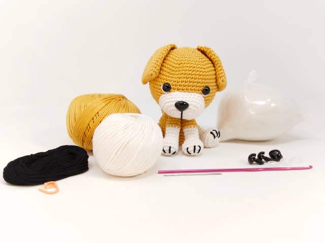 Crochet kit with Buddy Beagle pattern, featuring yarn in brown, white, and black, a crochet hook, and a cute beagle amigurumi.