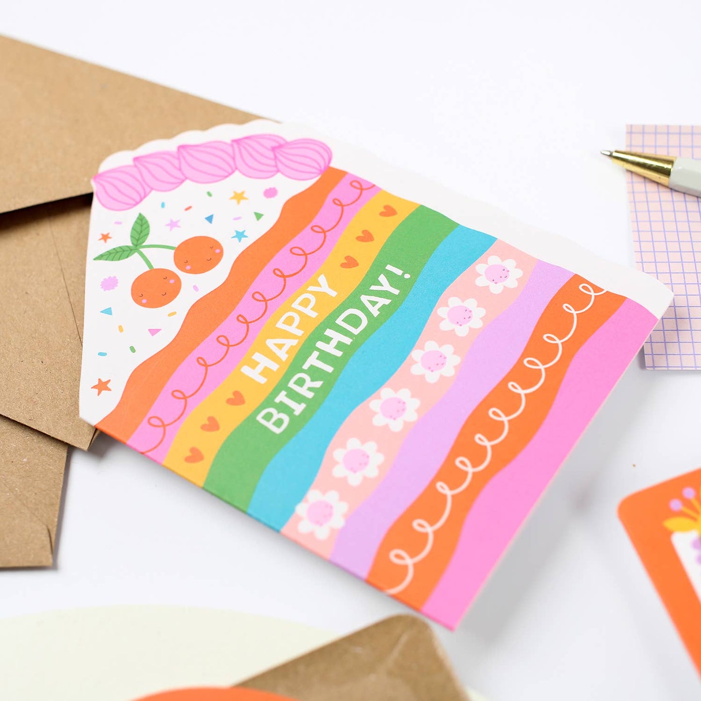A colorful, die-cut birthday card featuring a rainbow design with "Happy Birthday!" and cute cake details.