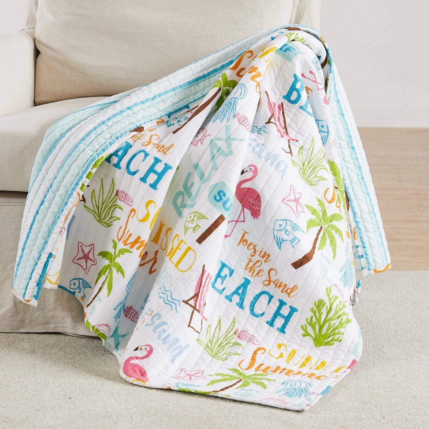 Colorful beach-themed quilted throw draped over a cream sofa