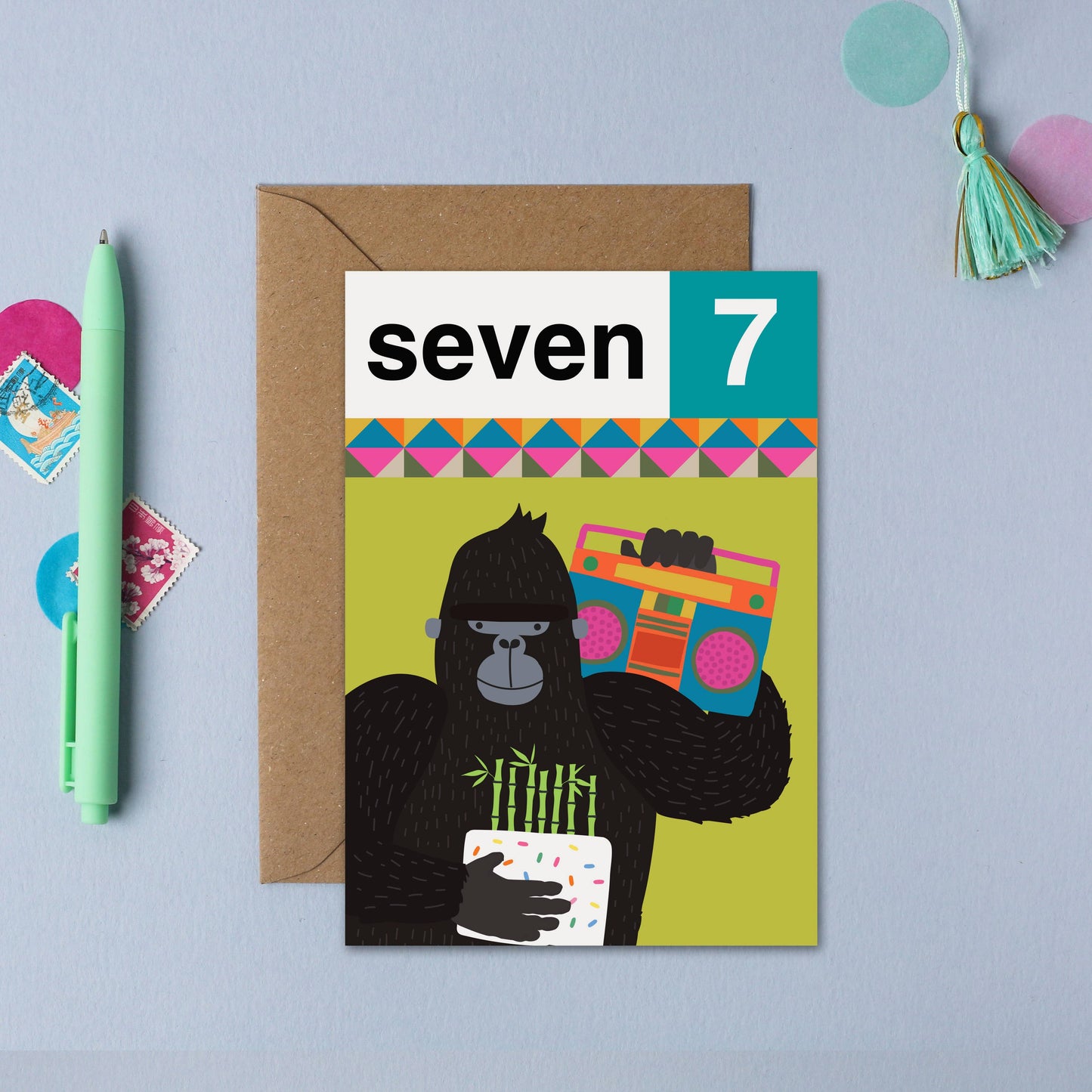 Fun 7th birthday card featuring a playful gorilla holding a cake and boombox, with colorful geometric patterns.