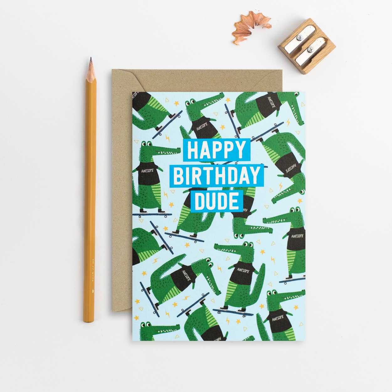 A handmade birthday card featuring a playful pattern of skateboarding crocodiles on a light blue background, with "Happy Birthday Dude" in bold letters.