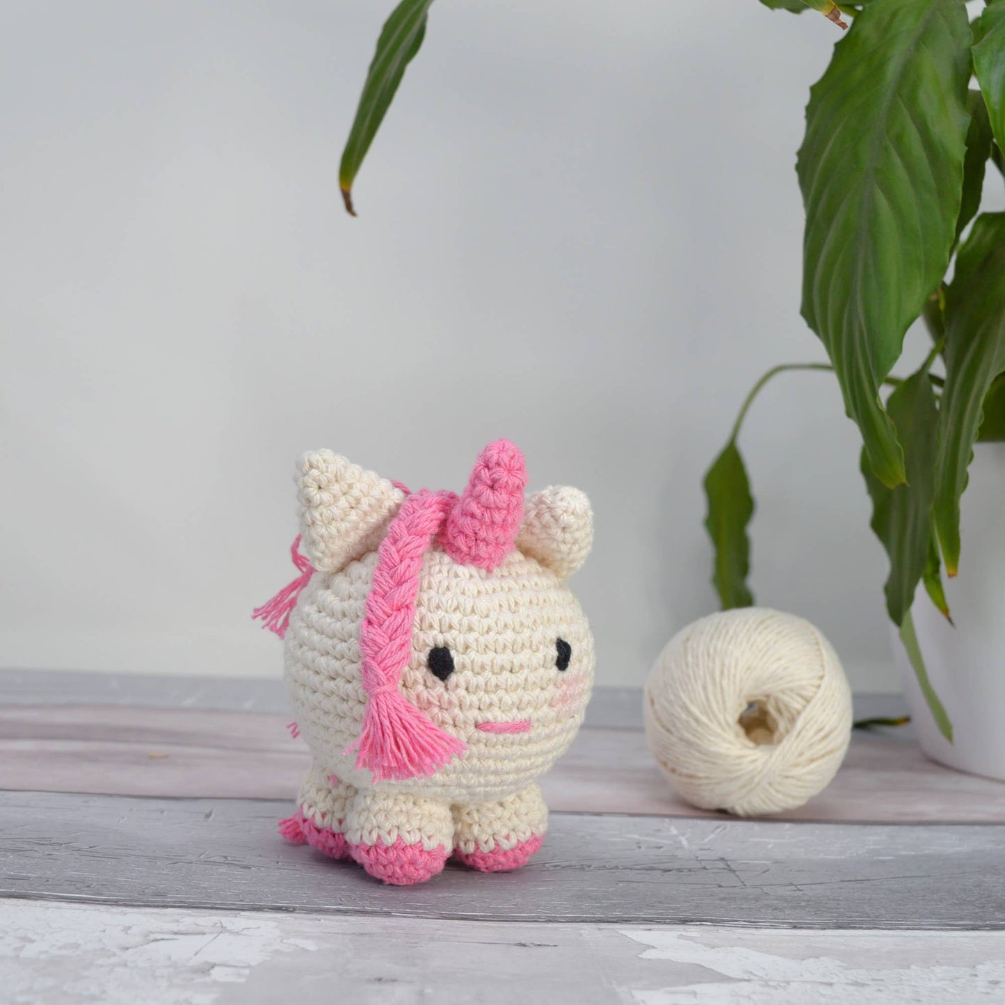 Small cream and pink crocheted unicorn plushie with yarn ball nearby.