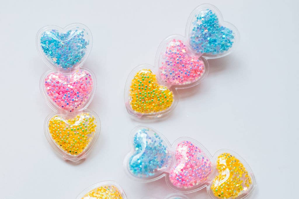 Clear heart-shaped hair clips filled with pastel sequins in pink, yellow, and blue, set on alligator clips.