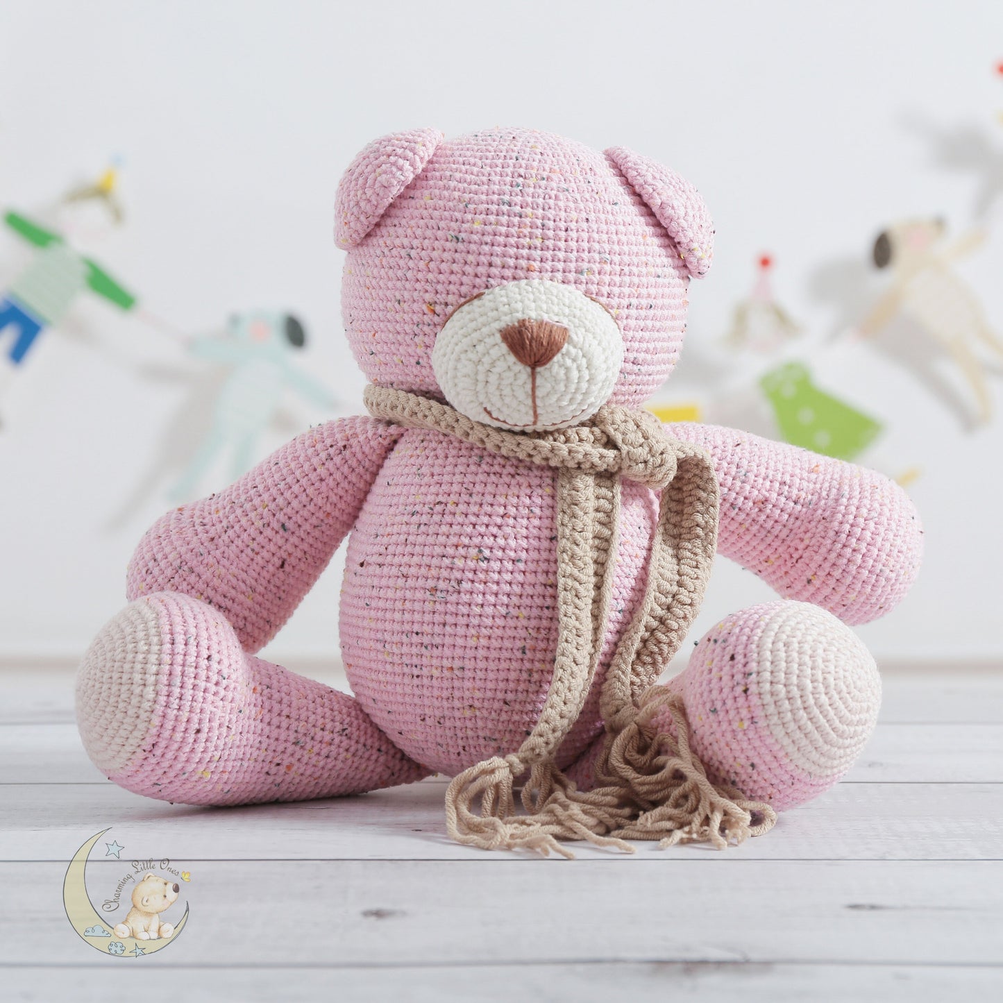 A handmade crocheted teddy bear in pink with a beige scarf, 13 inches tall.