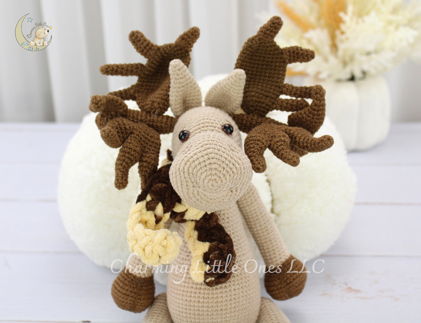 A handmade crochet Christmas stuffed moose with brown antlers, beige body, and yellow accents.