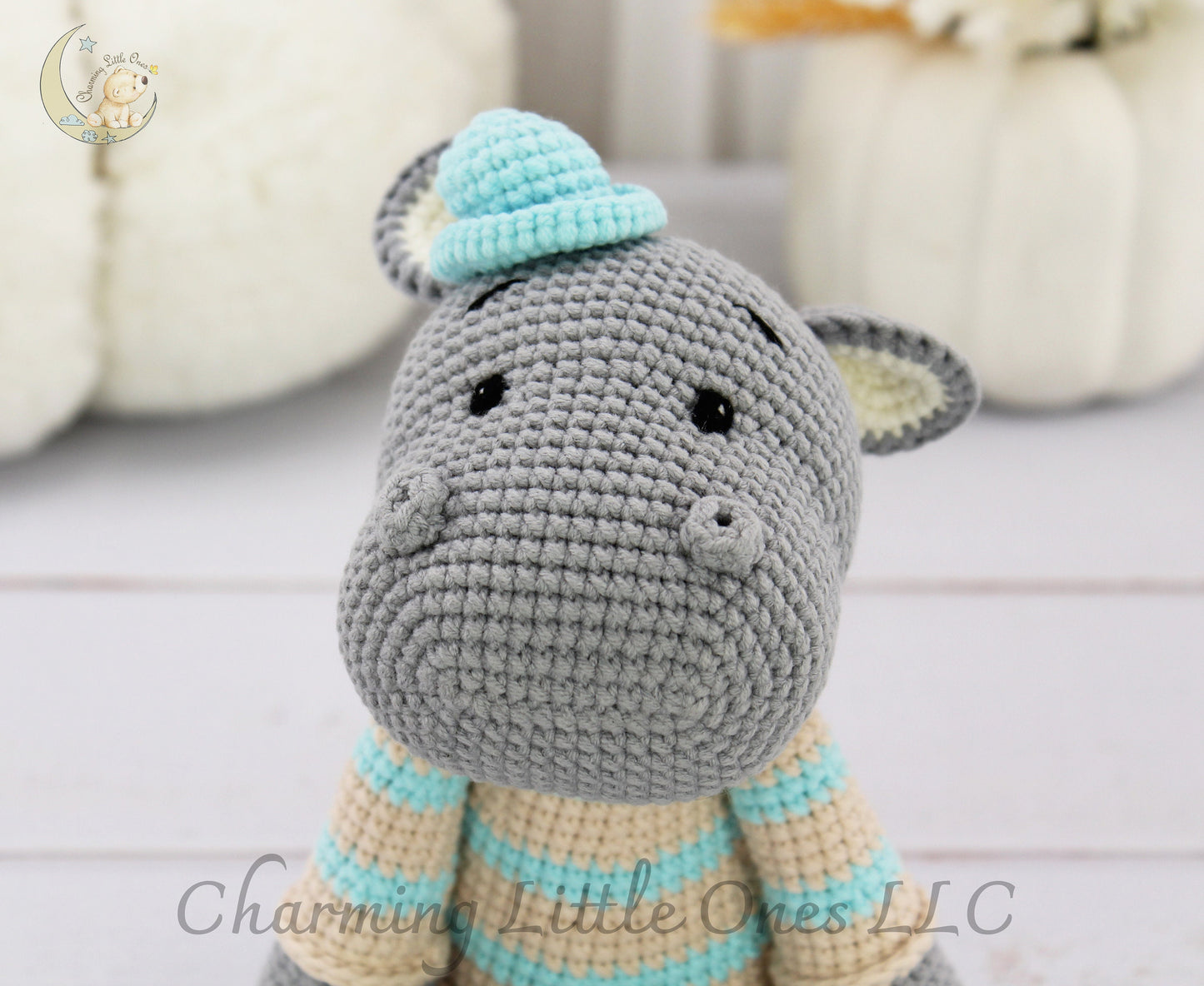Handmade crochet hippo with gray body, light blue hat, and striped scarf, perfect for cuddling.