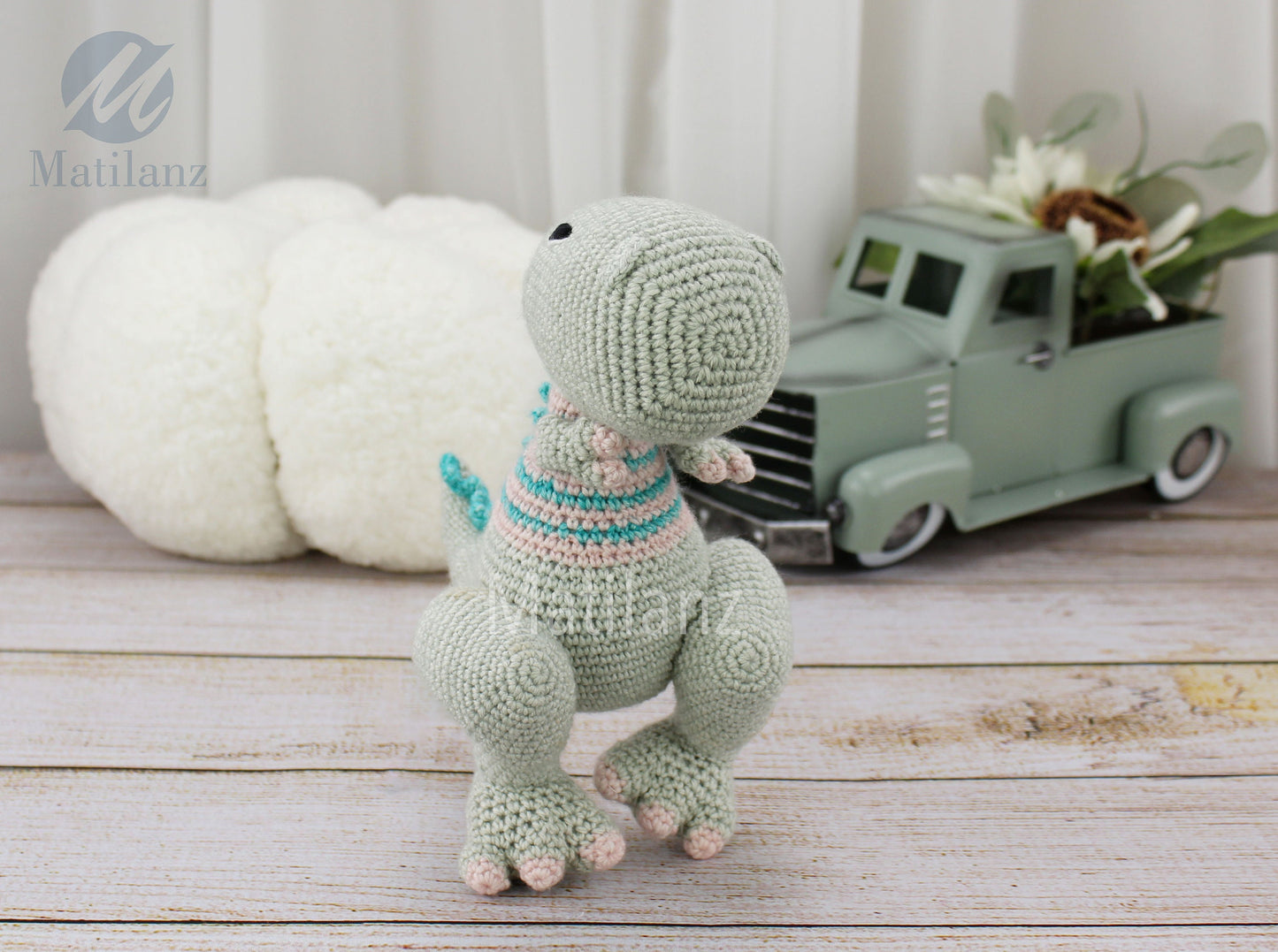 A handmade crochet TRex dinosaur toy in light green with a striped sweater, 8 inches tall.