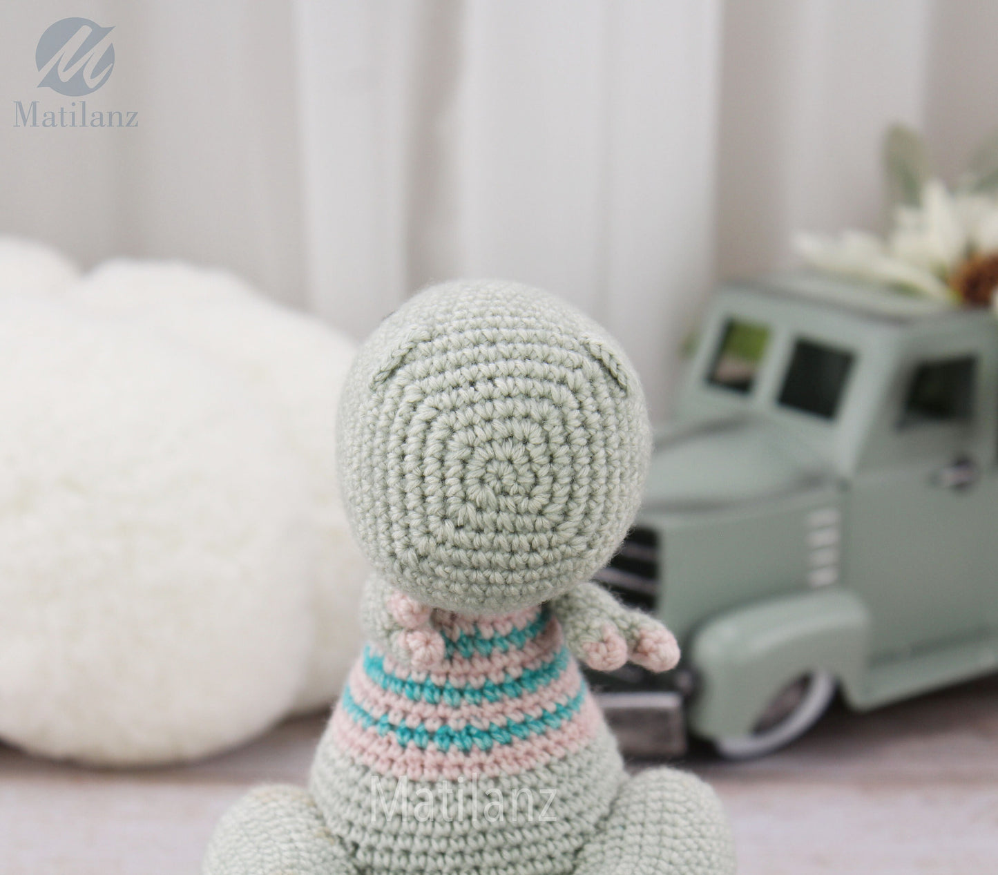 A handmade crochet TRex dinosaur toy with pastel green body and striped pink and blue sweater.