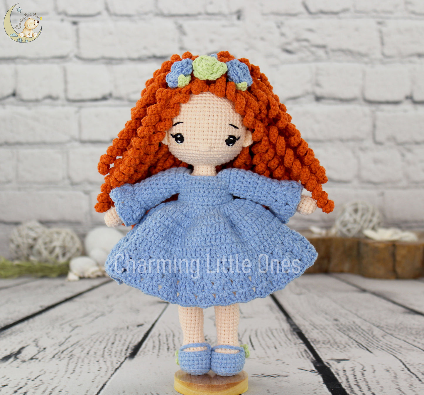 A handmade crochet doll with orange curly hair, blue dress, and flower crown, 10" tall.