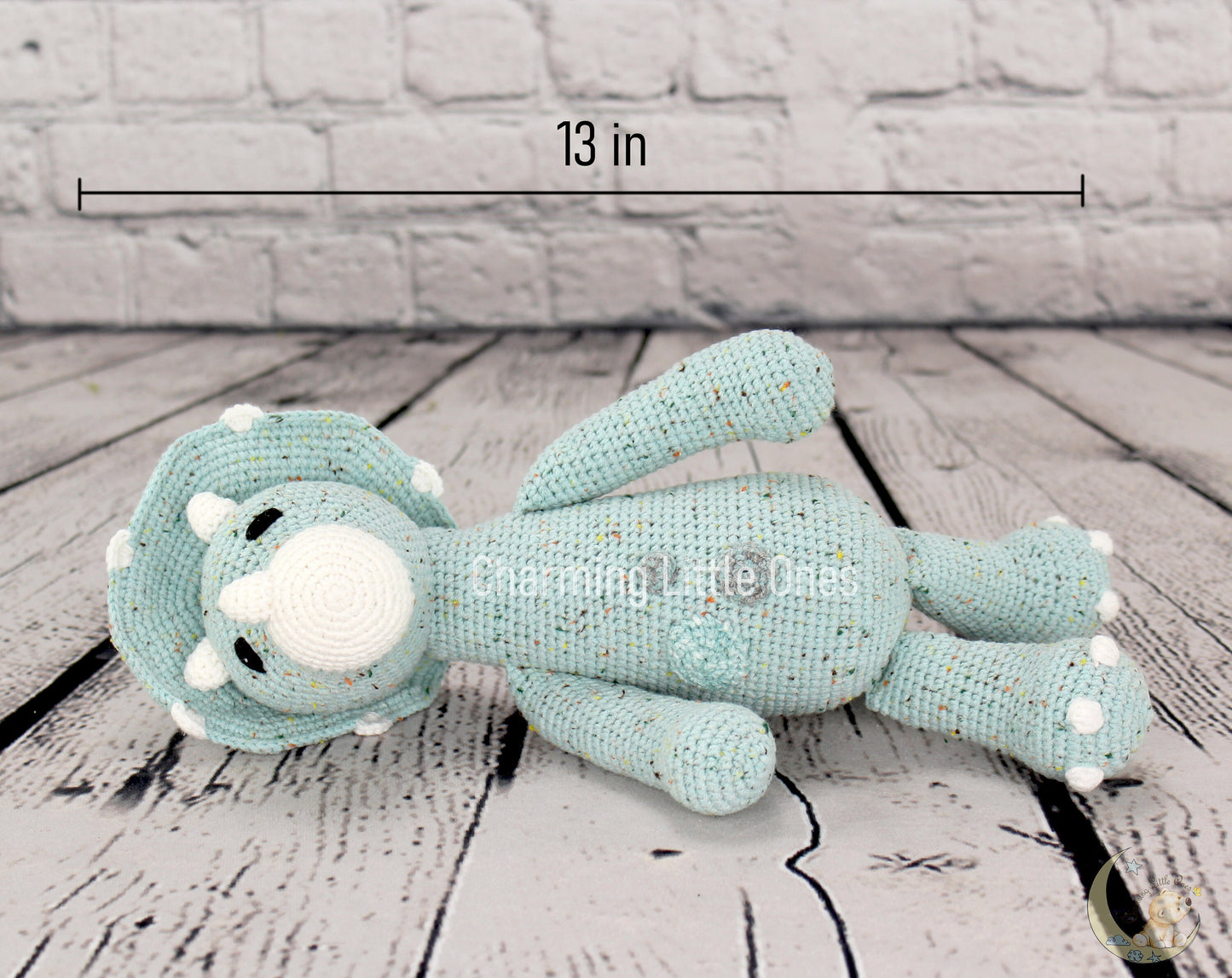 A handmade crochet Triceratops dinosaur toy in light blue with white accents, 12 inches long.
