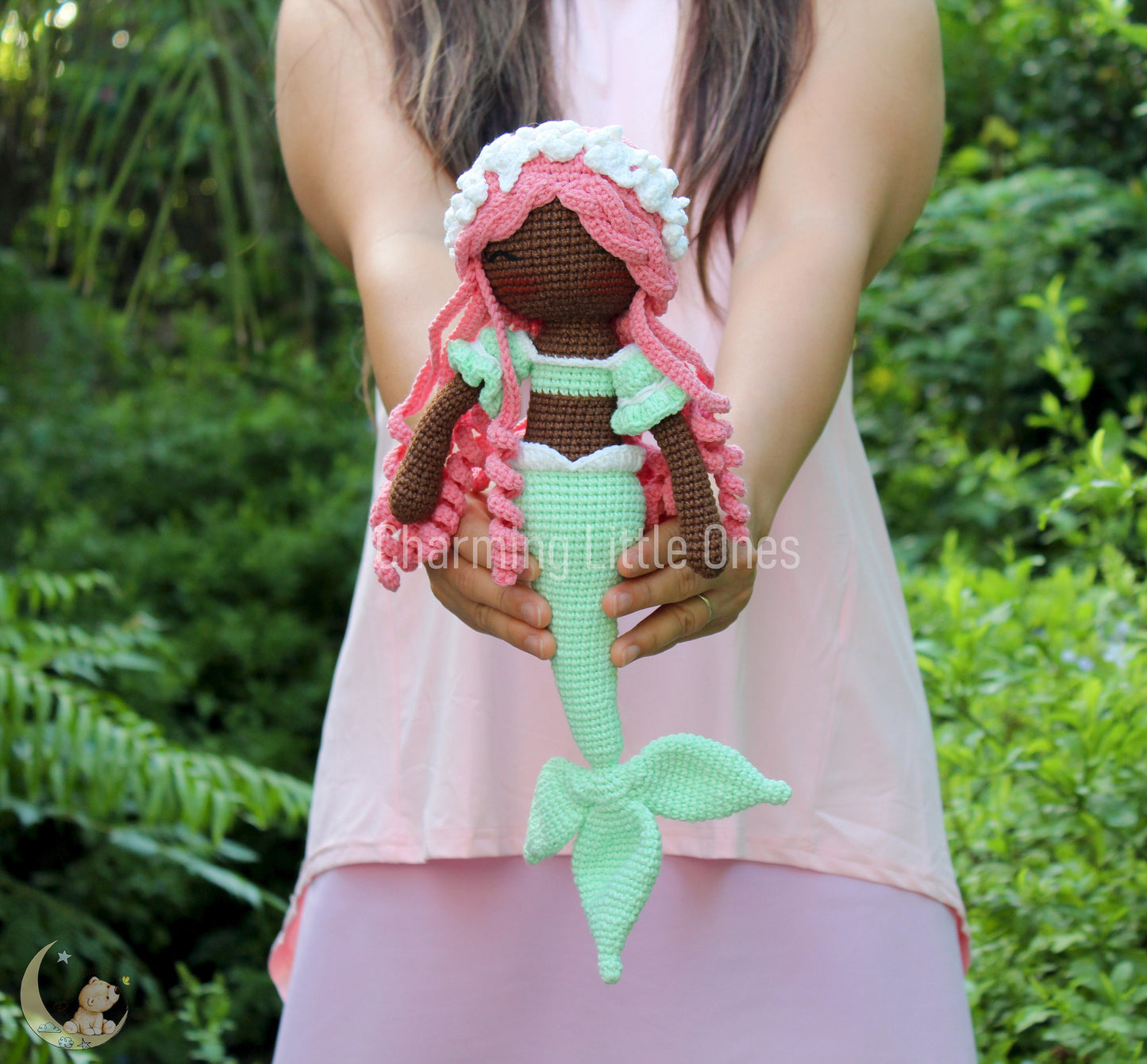 A handmade crochet mermaid doll with pink hair, green tail, and white accents.