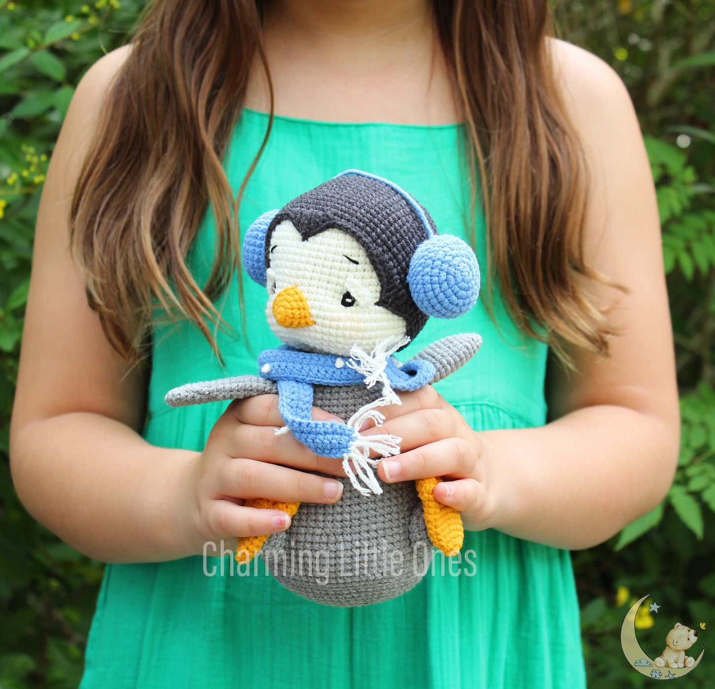 Handmade crochet penguin with gray body, white belly, blue hat, and scarf, featuring yellow feet and beak.