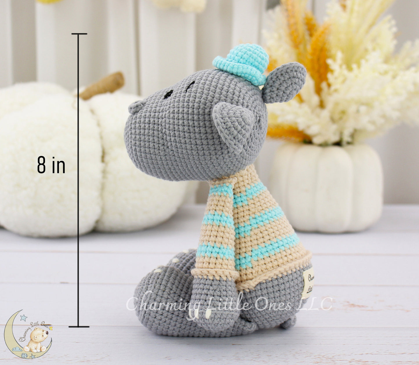 A handmade crochet hippo toy in gray with a blue hat and striped scarf, 11 inches tall.