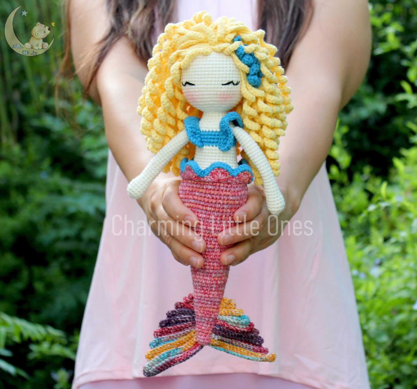 A handmade crochet mermaid doll with blonde hair, blue top, pink tail, and closed eyes.