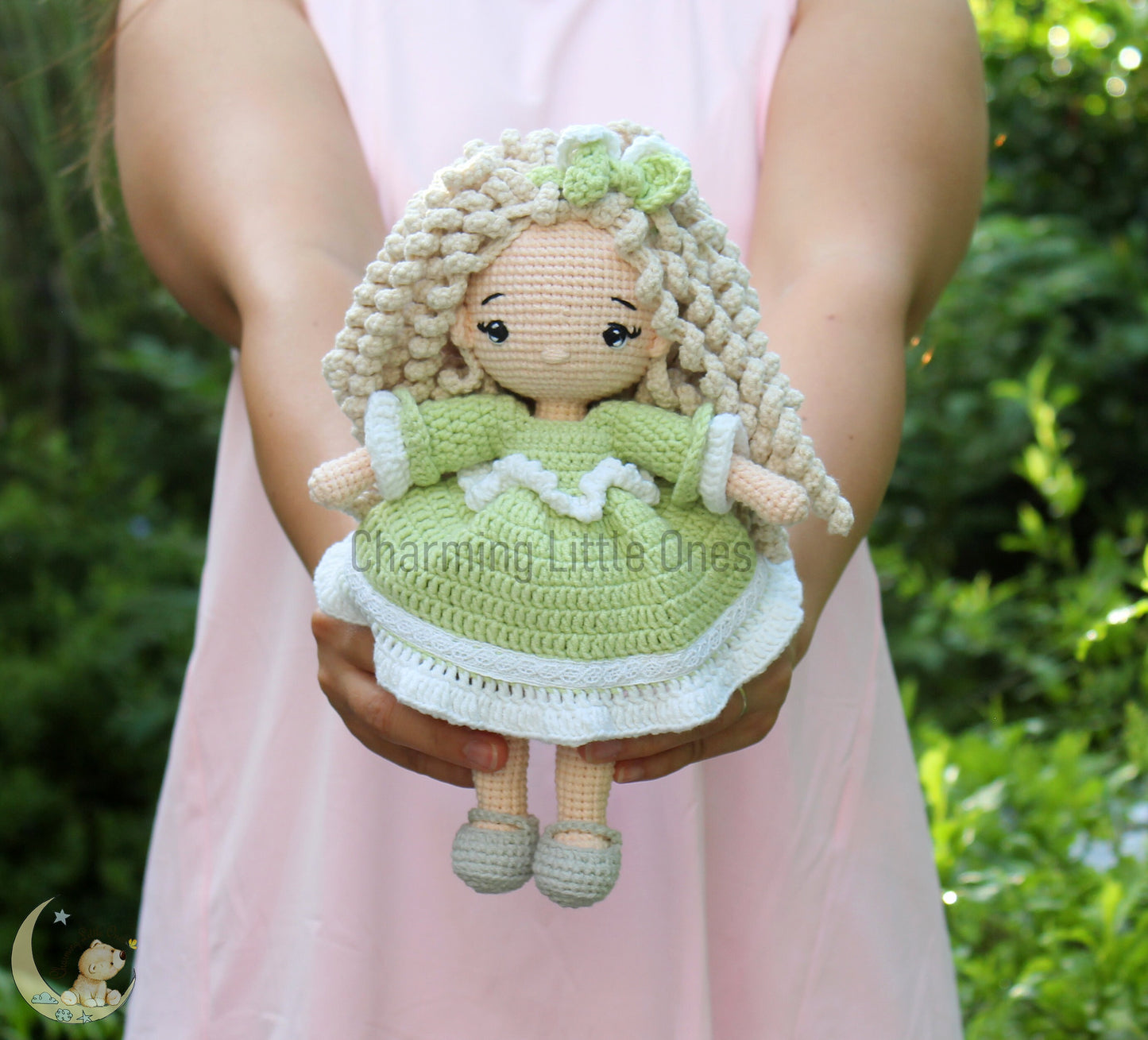 A handmade crochet doll with curly blonde hair, wearing a green dress and white shoes.