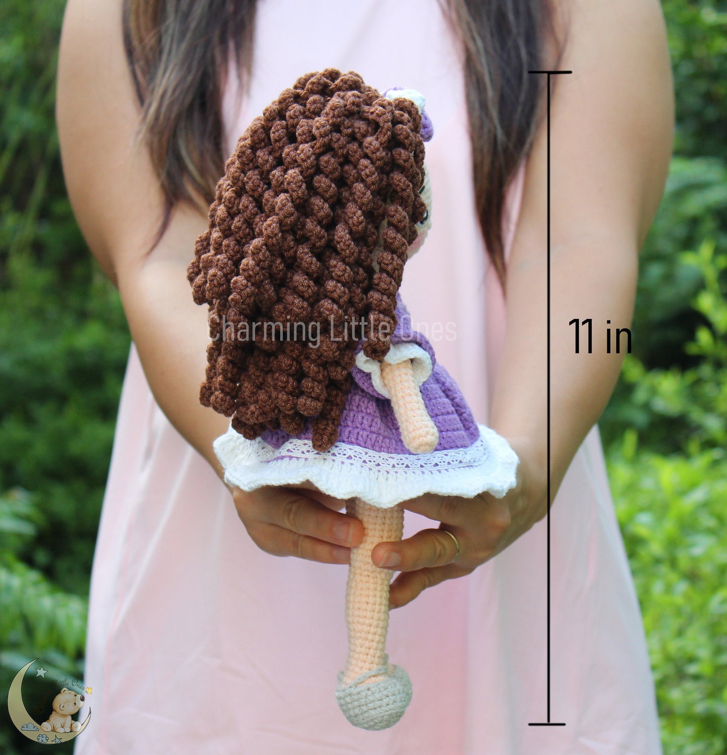 A handmade crochet doll with long brown hair, wearing a purple dress and white lace trim.