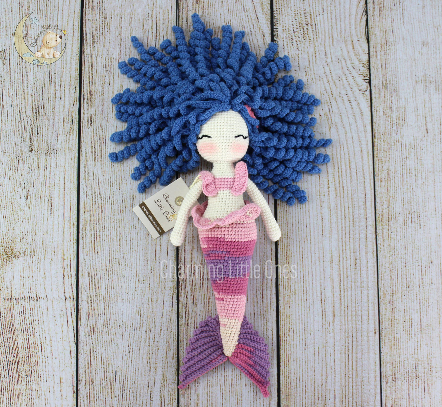 A handmade crochet mermaid doll with blue hair, pink and purple striped tail, and a white top.
