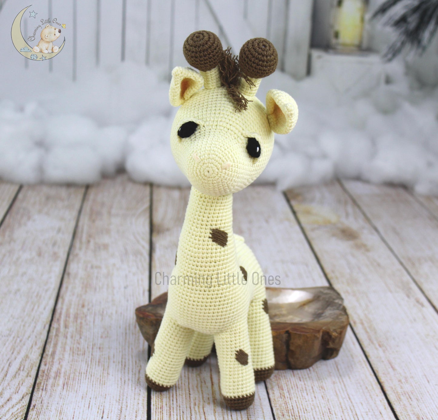 A handmade crochet giraffe with brown spots and tufted horns, standing on a wooden block.