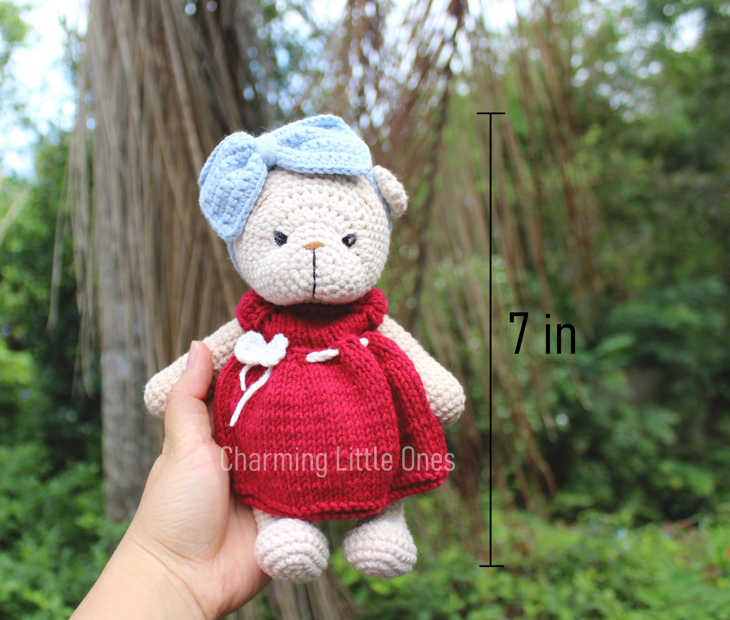 A handmade crochet Christmas bear wearing a red dress and blue bow, 7 inches tall.