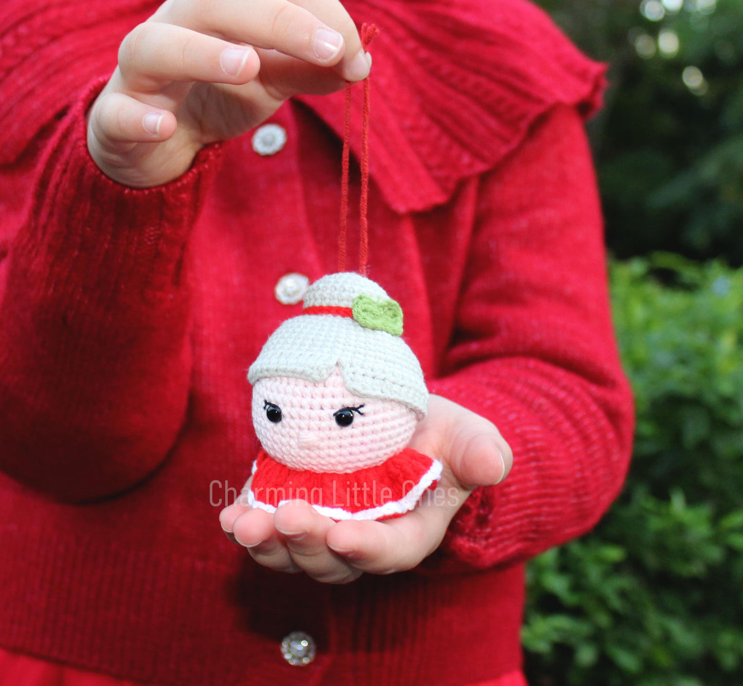 Person holding a small crocheted ornament with a red sweater outdoors