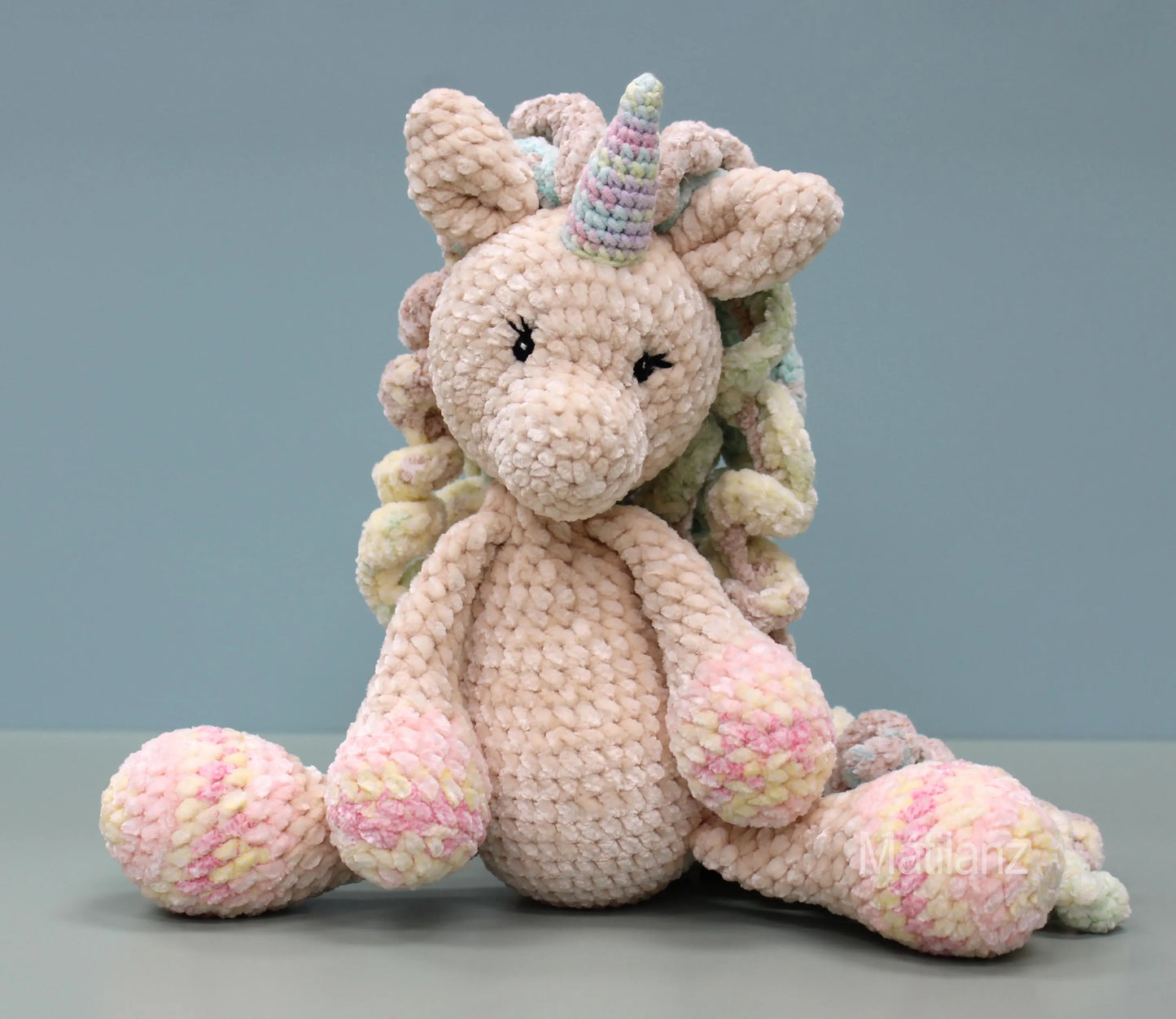 Hand-crocheted plush unicorn with rainbow mane and pink hooves