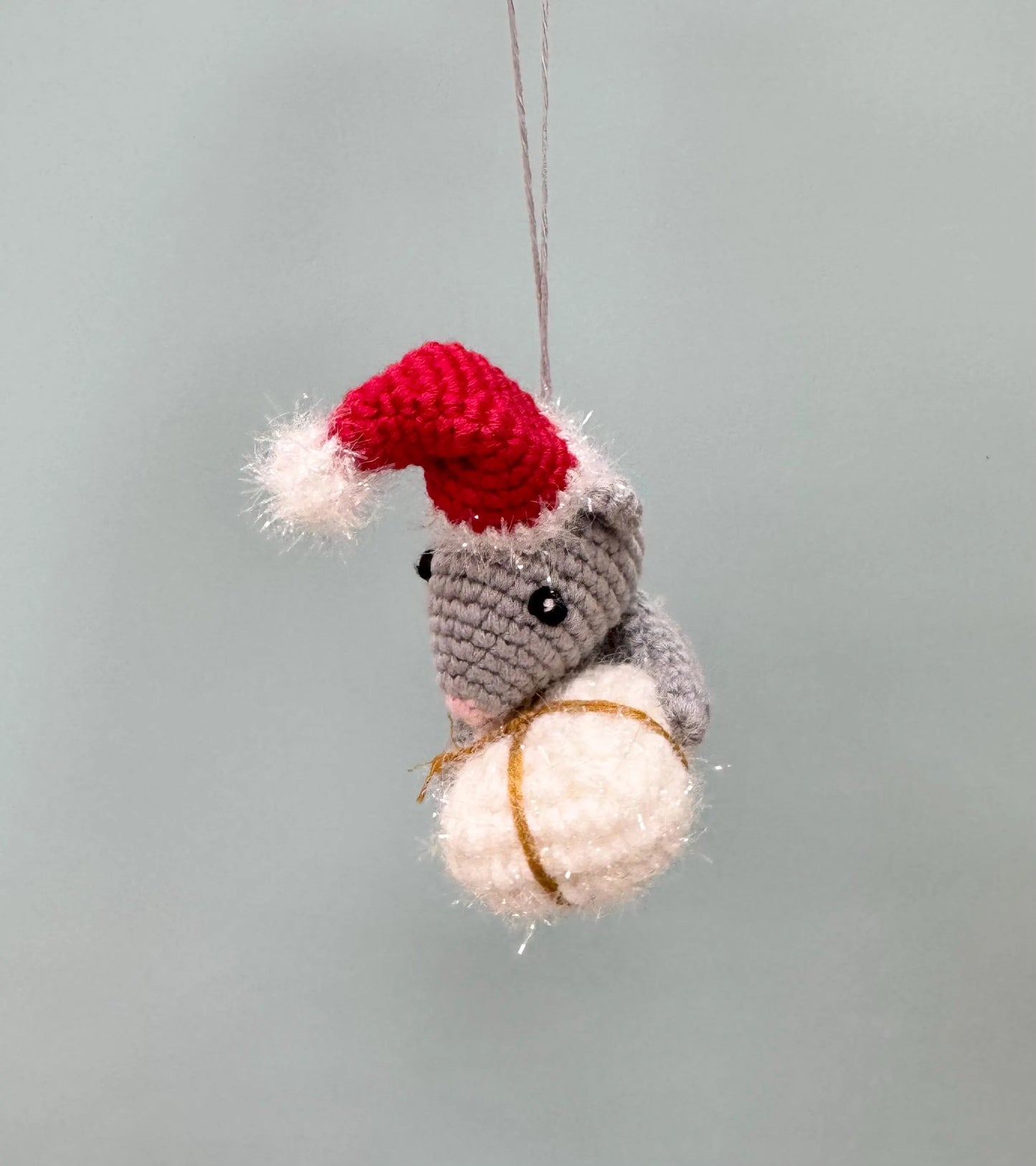 Crochet mouse ornament in gray with a red Santa hat, holding a white present.