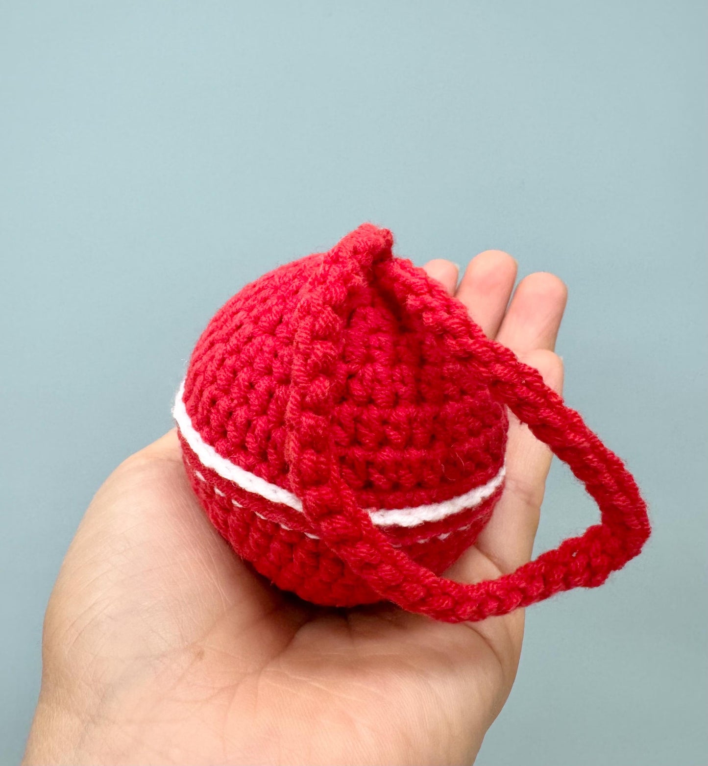 Handmade red crochet Christmas ball with white stripes and a loop for hanging.