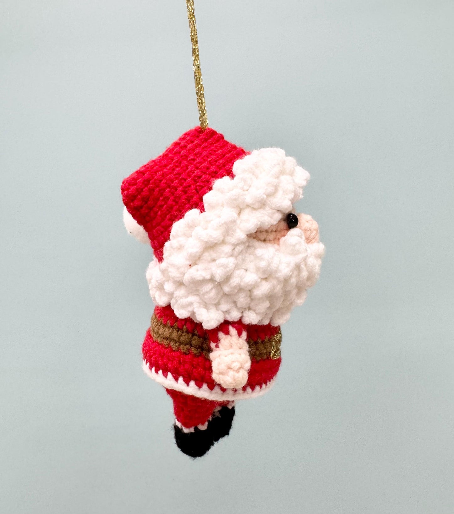 Crochet Santa Claus ornament with a red hat and suit, white beard, and black boots, perfect for holiday decorating.