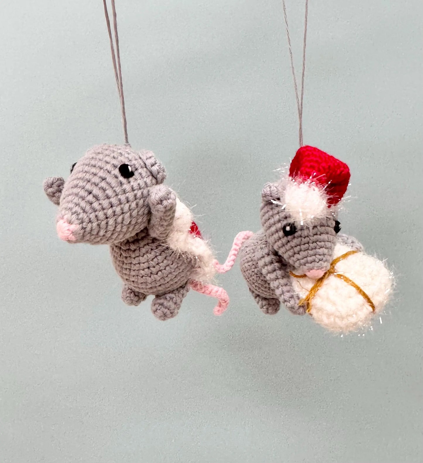 Crochet mouse ornament holding a Christmas present, gray with red hat, handmade festive decoration.