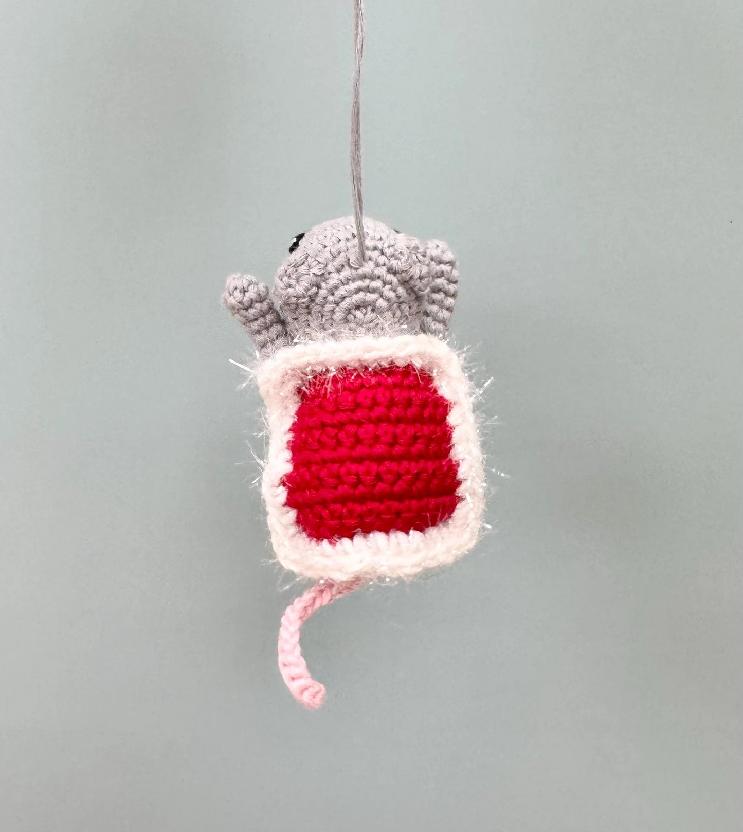 Crochet mouse ornament holding a red present, perfect for Christmas tree decoration.