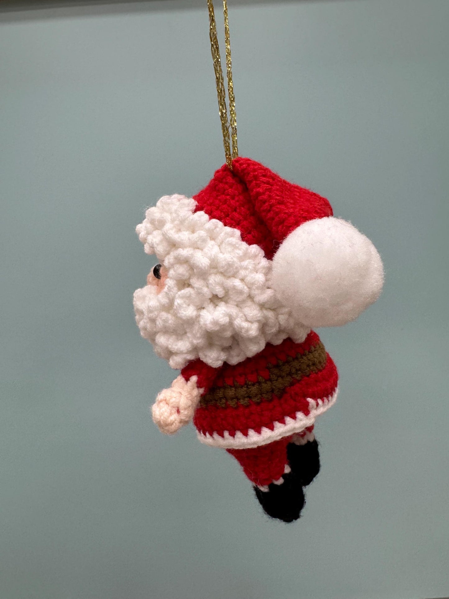 Crochet Santa Claus ornament with red and white outfit, fluffy white beard, and gold hanging string.