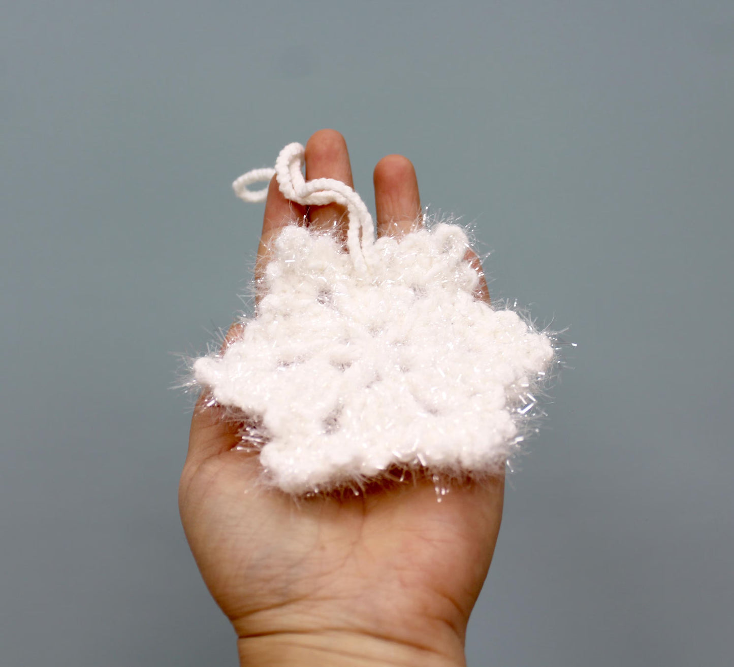 A fluffy white crochet snowflake Christmas ornament with a loop for hanging.