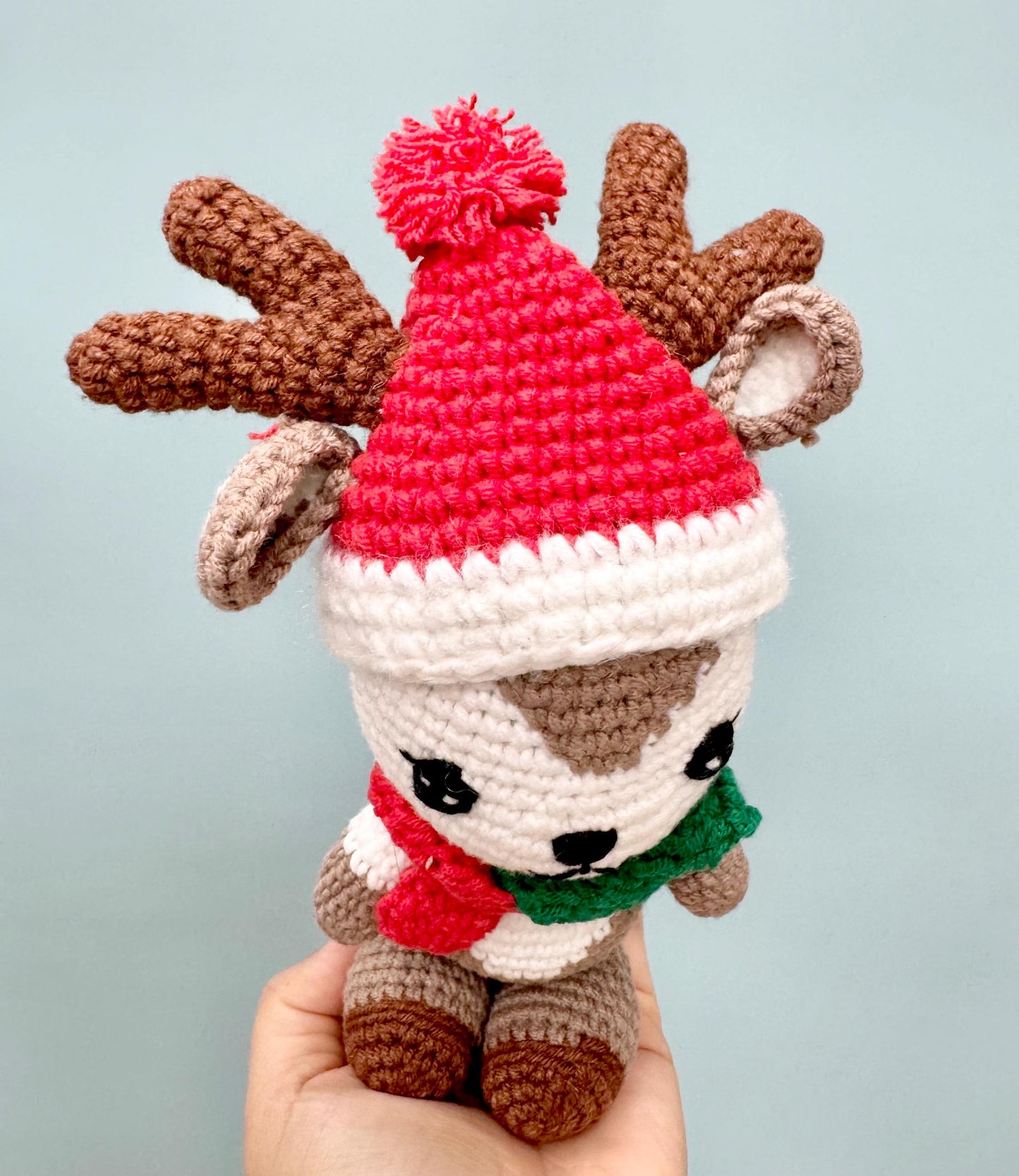 Crochet reindeer plush with brown antlers, red Santa hat, and festive scarf, perfect for Christmas.