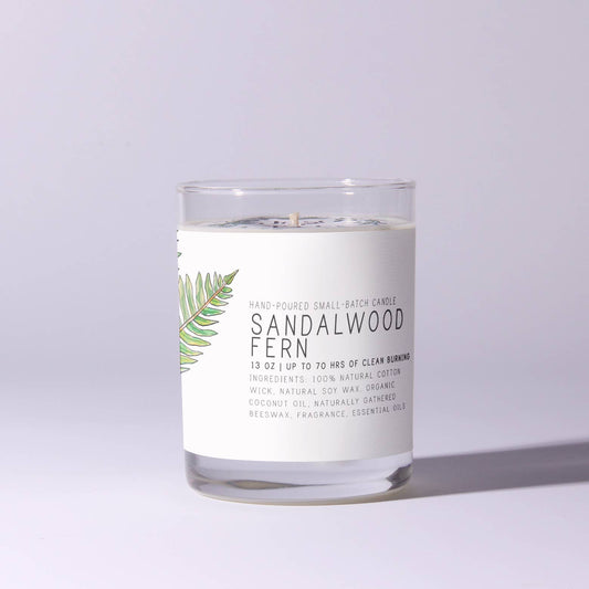 Glass candle labeled Sandalwood Fern with illustrated green leaves on label