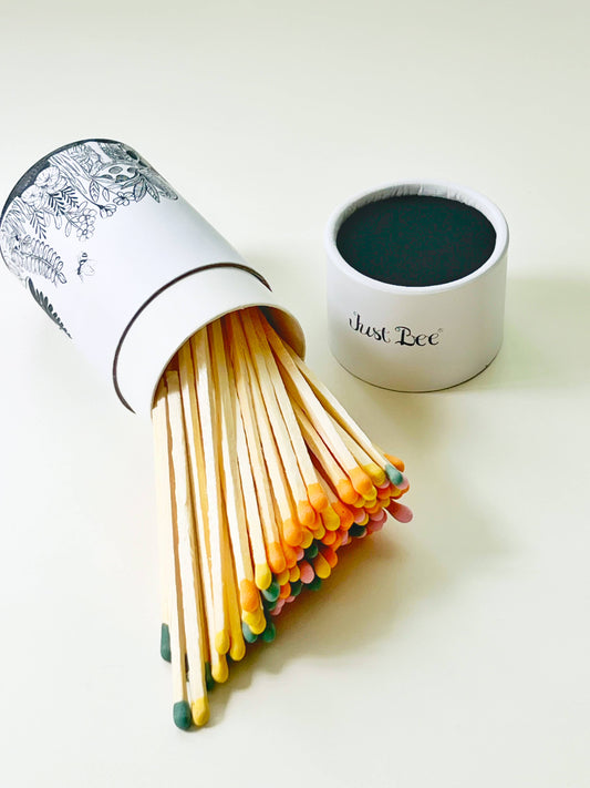 Stylish tube of long pastel-colored safety matches spilling onto a white surface with botanical detail.