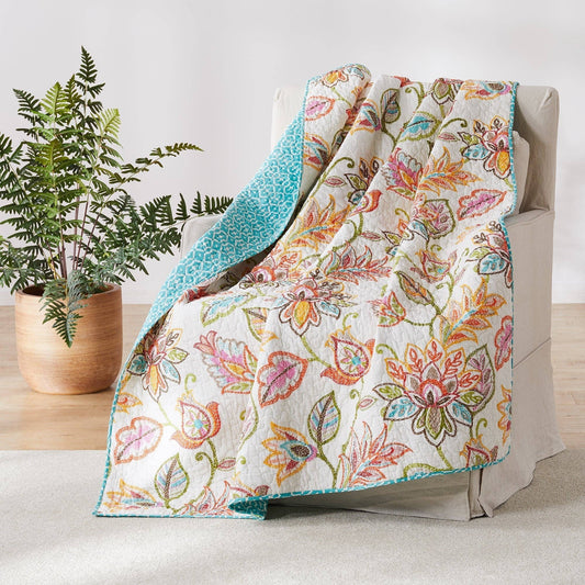 Colorful floral quilted throw draped over a beige armchair with teal reverse side