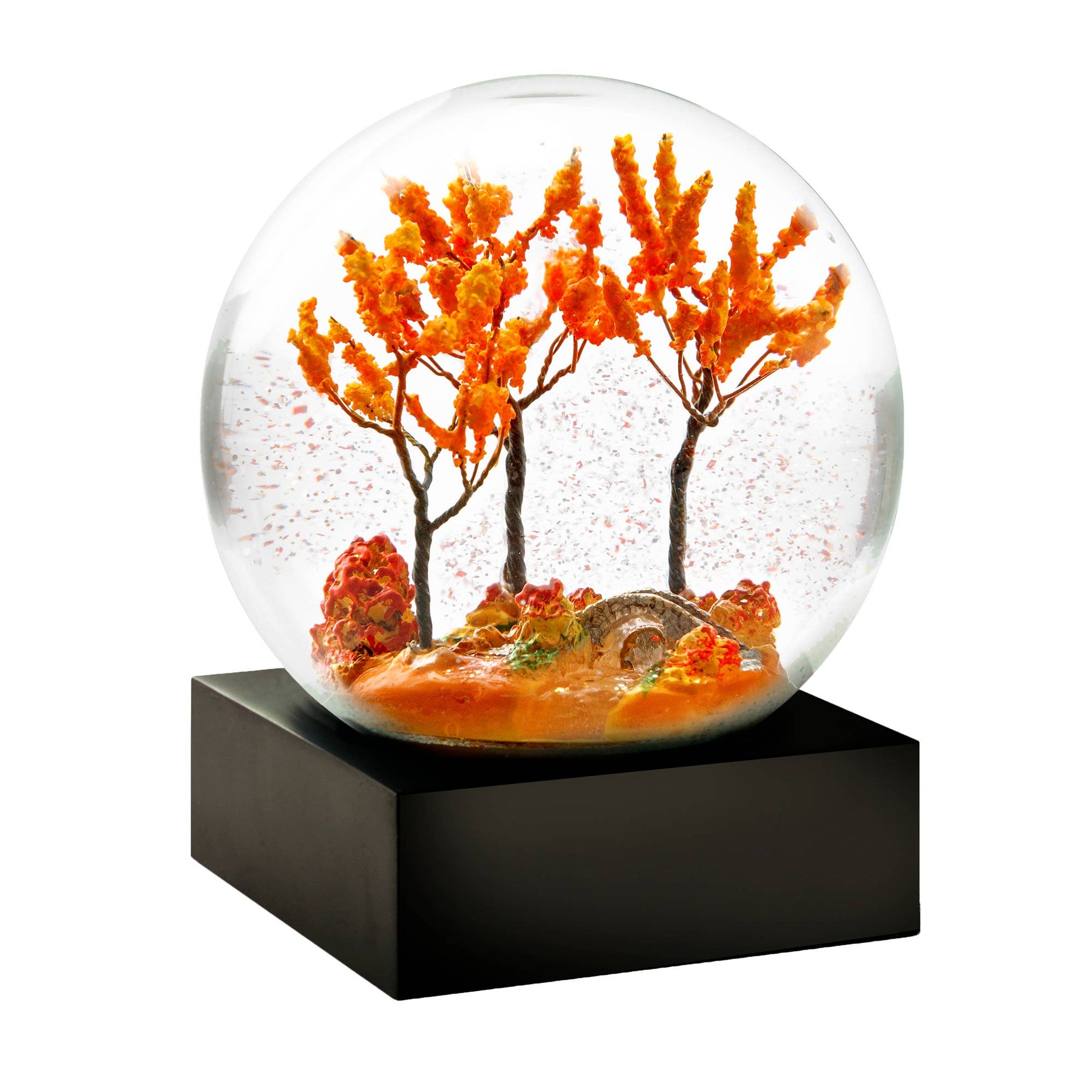 Glass snow globe with autumn trees and a miniature stone bridge on a black base