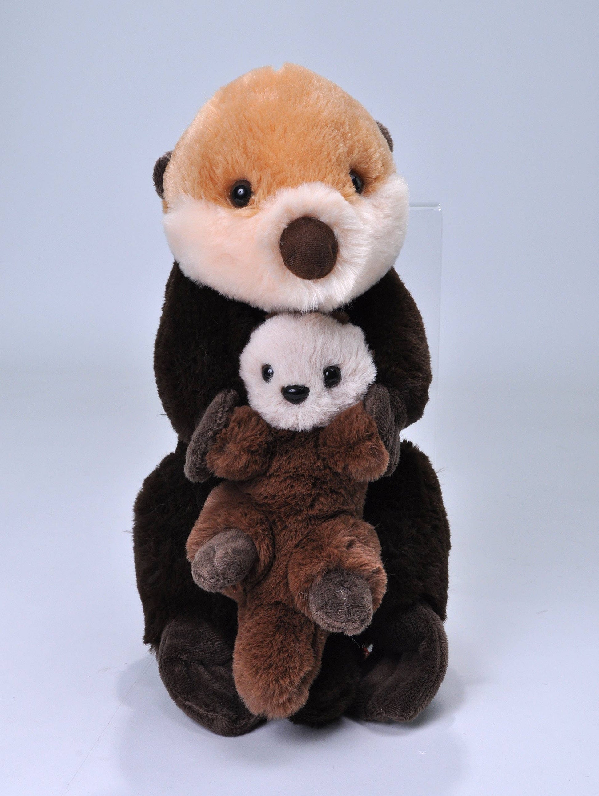 Brown sea otter plush holding a smaller baby otter, both with soft fur and cuddly designs.