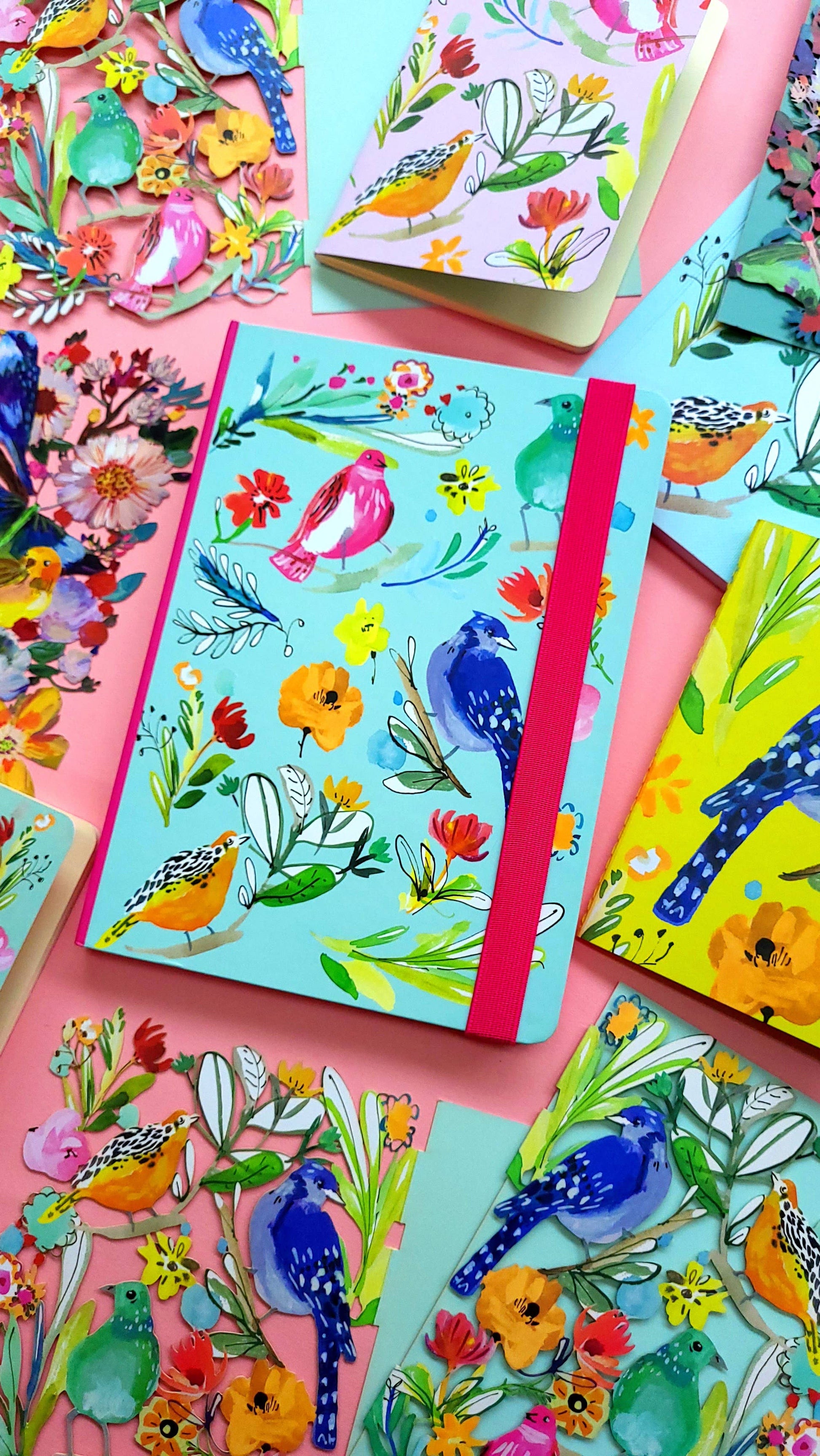 A5 journal with colorful bird and floral artwork, featuring a red elastic binder.