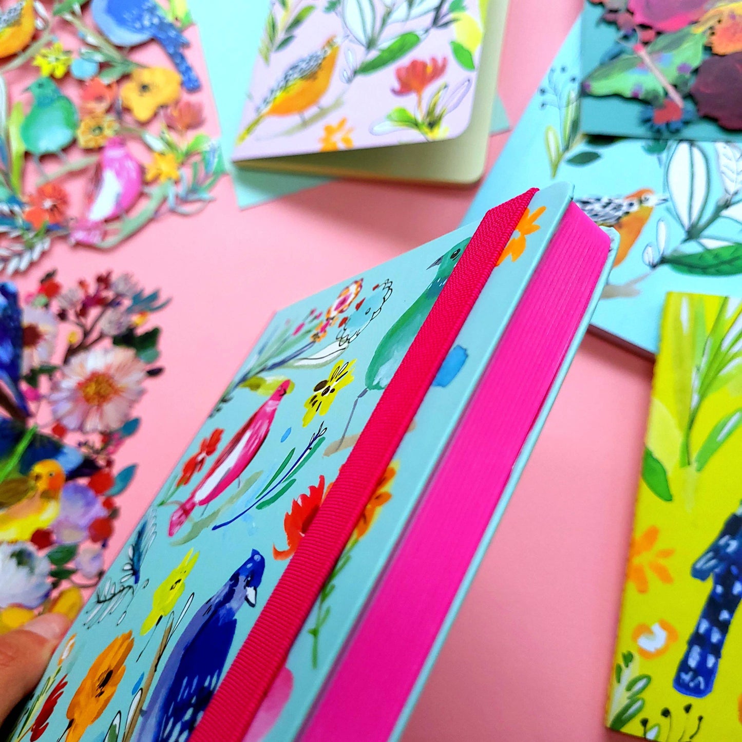 A5 journal with colorful bird and flower artwork, featuring a pink elastic binder.