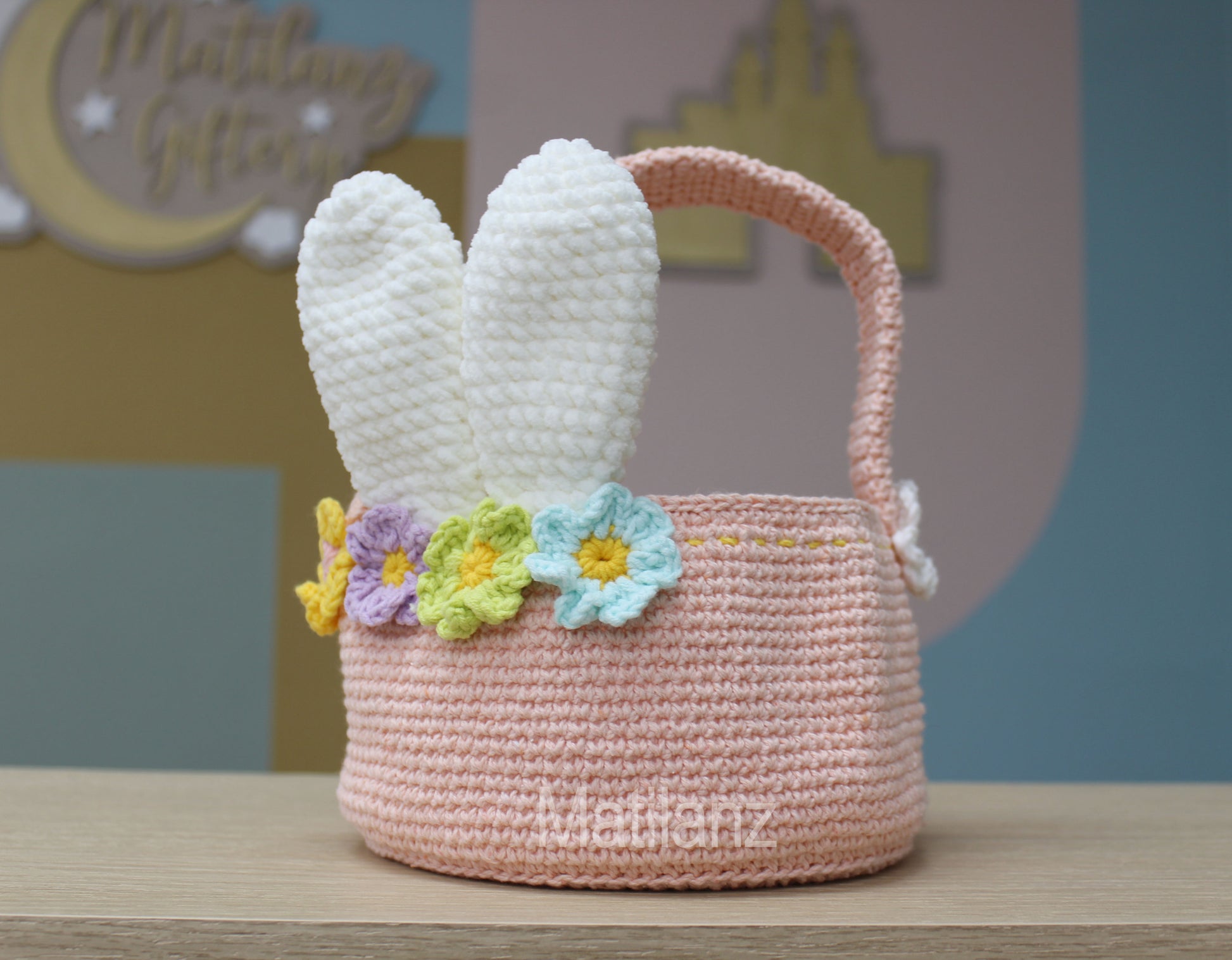 A handmade crochet Easter bunny basket with pastel pink color, white bunny ears, and colorful flower trim.