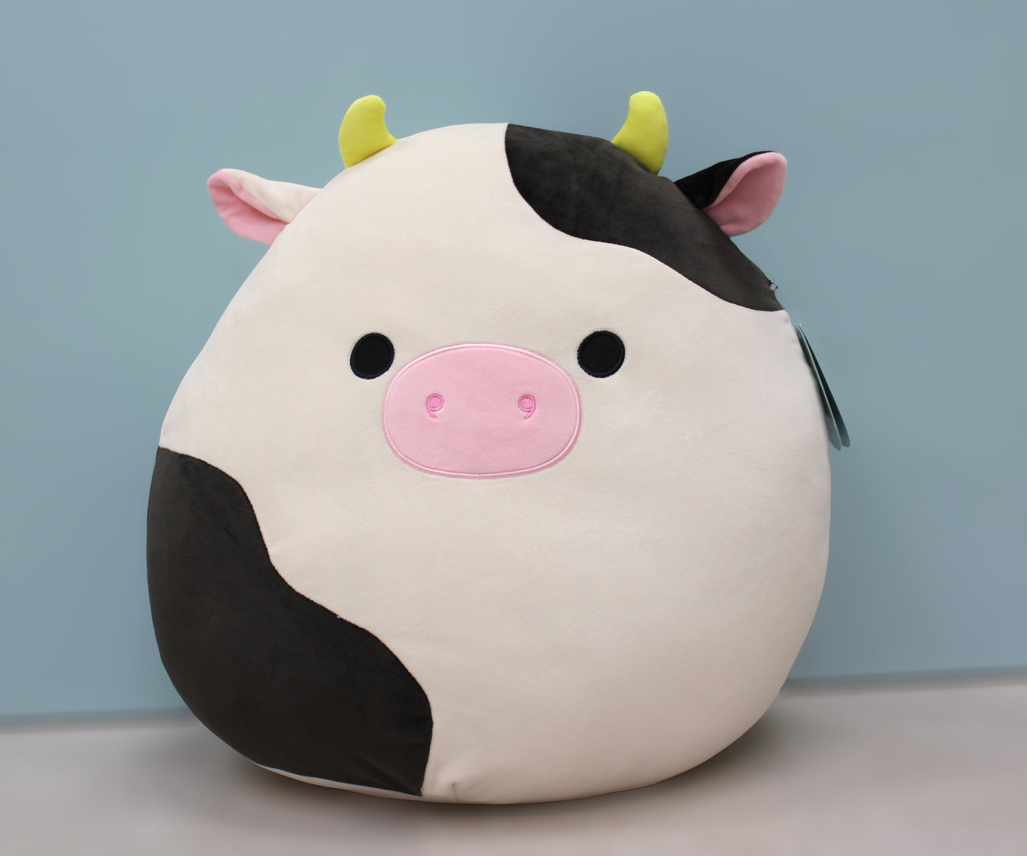 A large, soft cow plush with black and white spots, pink nose, and yellow horns.