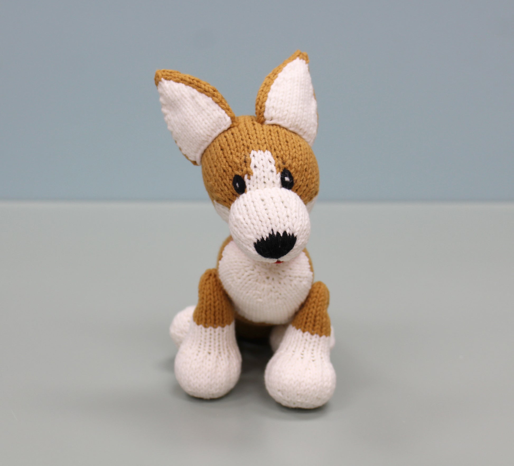 Brown and white handmade knitted corgi plush toy with perked ears and a friendly expression.