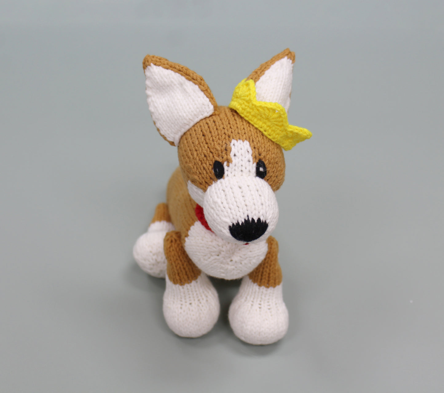Brown and white handmade knitted corgi plush with a yellow bow and red collar.