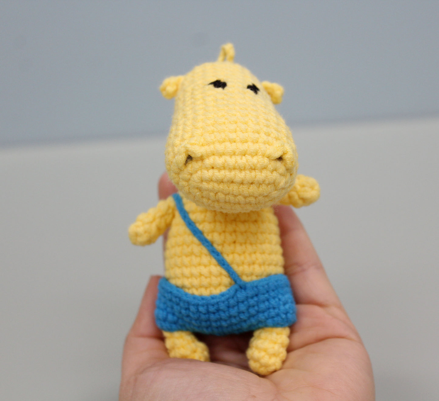 A yellow handmade crochet hippo keychain with a blue pouch, held in hand.