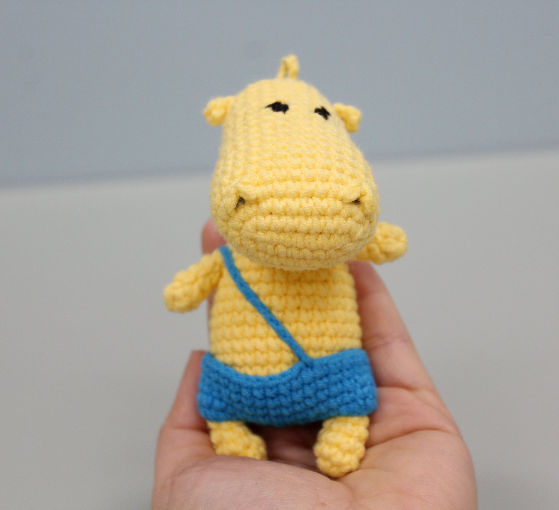 A yellow handmade crochet hippo keychain with a blue pouch, held in hand.