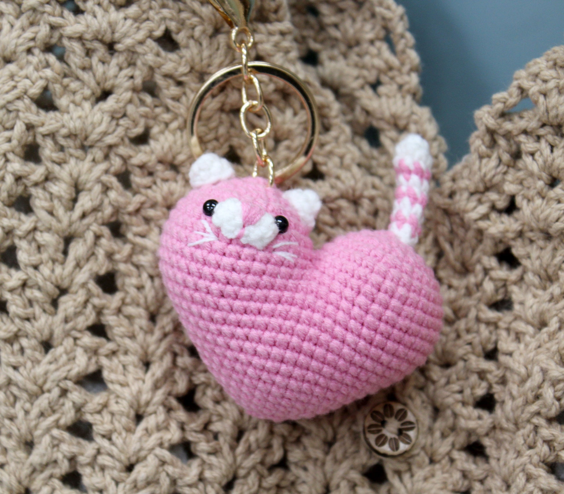 Pink and white crochet heart-shaped cat keychain with gold ring, featuring detailed facial and tail textures.