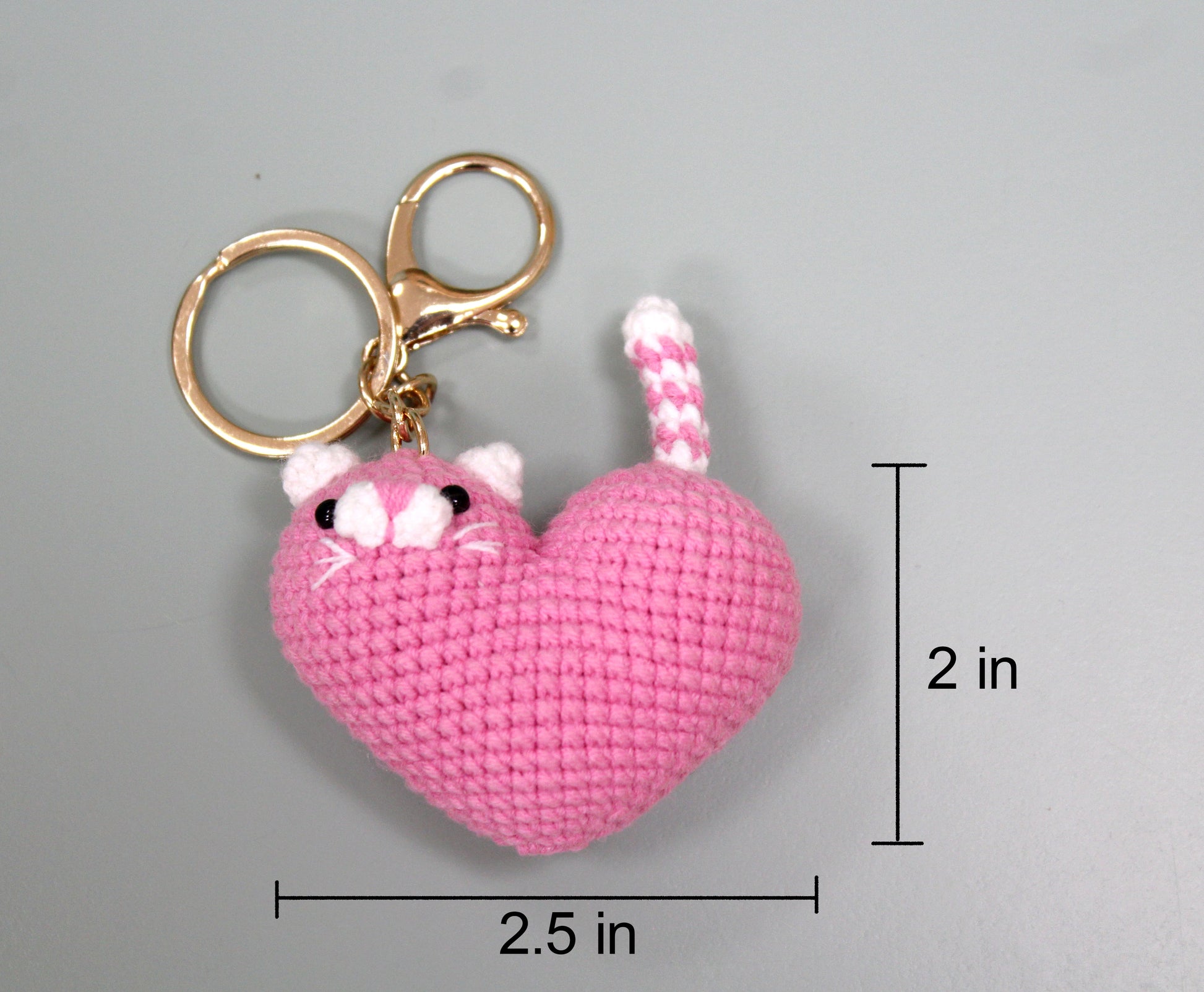 Pink crocheted heart-shaped cat keychain with white accents, measuring 2.5 inches wide and 2 inches tall.