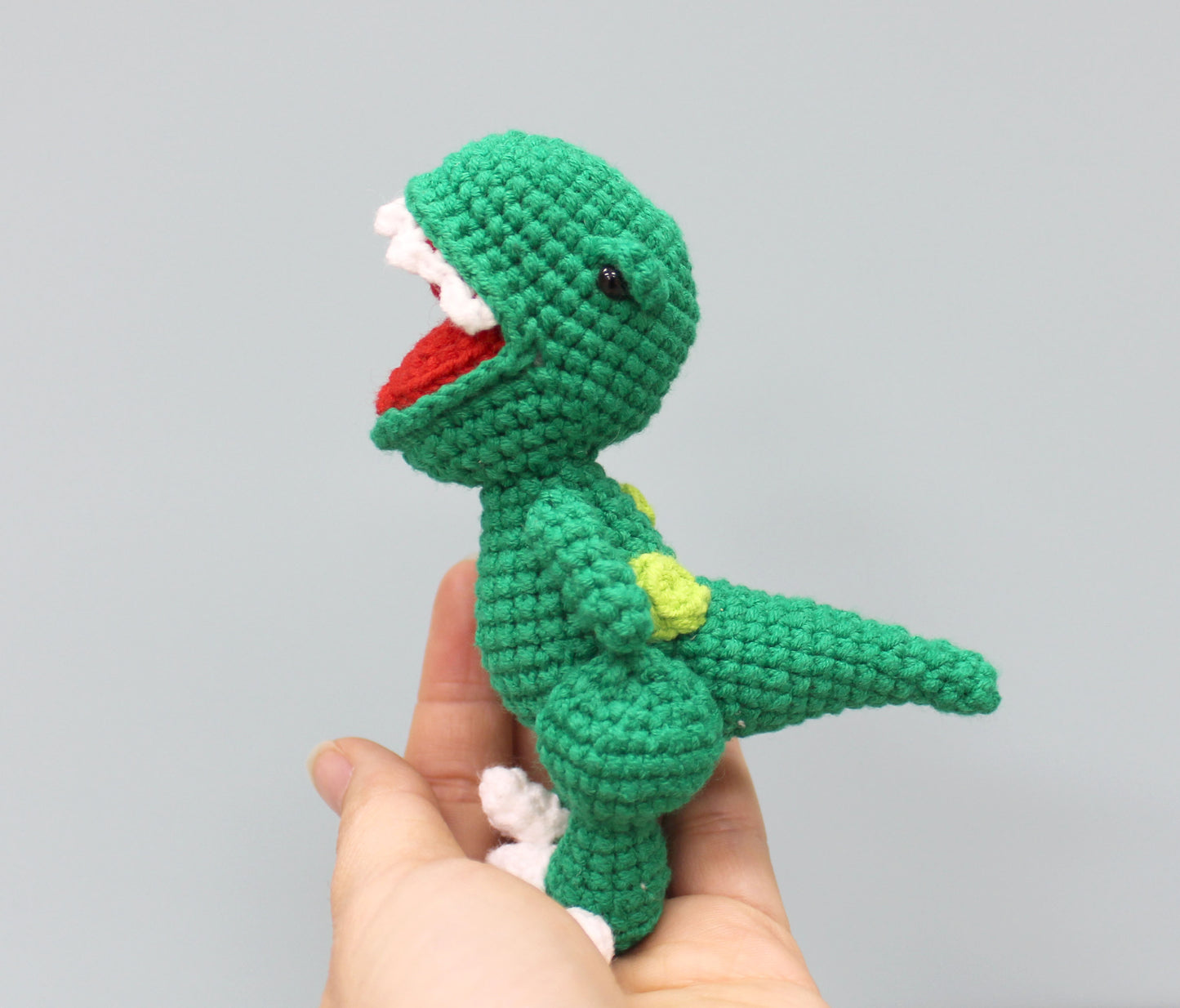 A green crocheted dinosaur keychain with a red mouth, white teeth, and yellow spots.