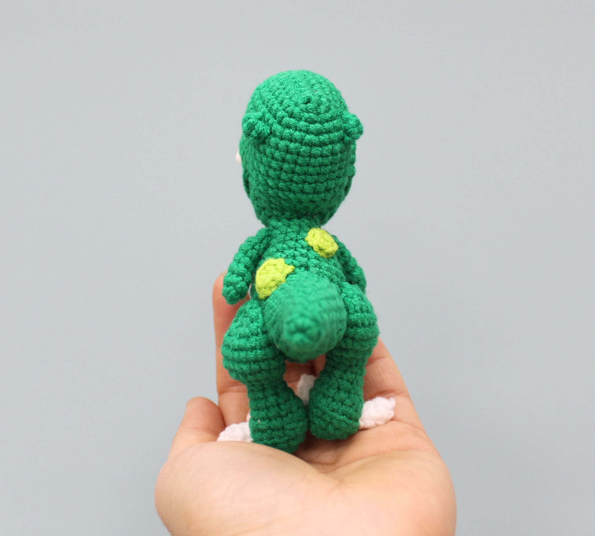 A small green crochet dinosaur keychain with yellow spots and white teeth.